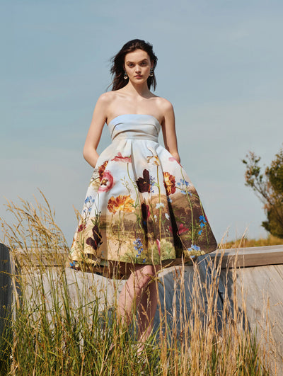 A model is posing in the grass wearing an Oscar de la Renta floral strapless cocktail dress. 