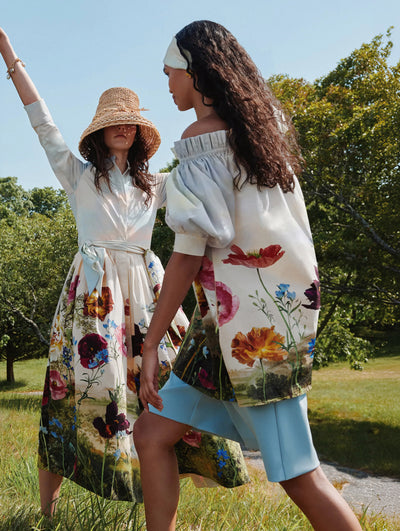 Two models are seen frolicking in the grass in floral cotton poplin ready-to-wear styles. 