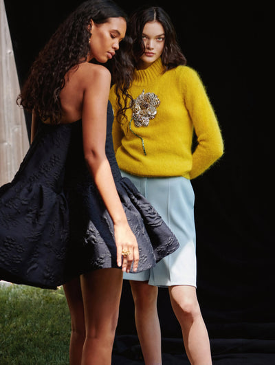 Two models are in frame. One is wearing an Oscar de la Renta navy cocktail dress and the other is wearing an Oscar de la Renta yellow sweater and blue short. 