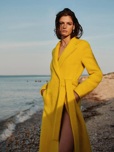 A model is wearing a yellow Oscar de la Renta coat on the beach. 