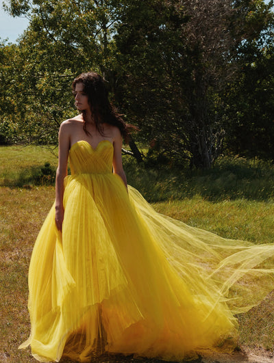 A model is posing in the grass wearing a yellow Oscar de la Renta strapless tulle gown. 