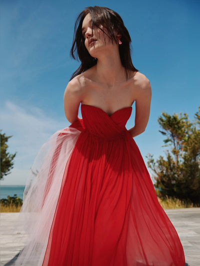 A model is posing outside in a red tulle Oscar de la Renta gown. 