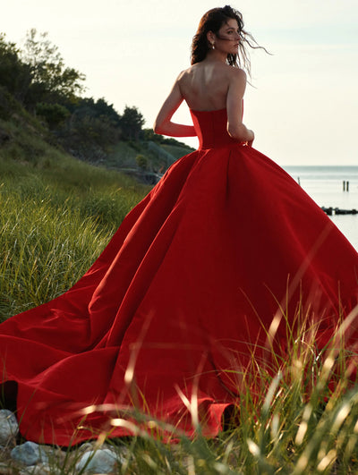 A model poses in a red Oscar de la Renta ballgown outside in grass. 