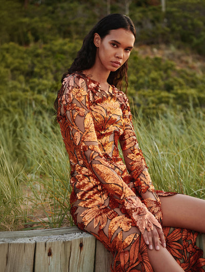 A model is seen sitting down in a laser cut metallic eveningwear dress.