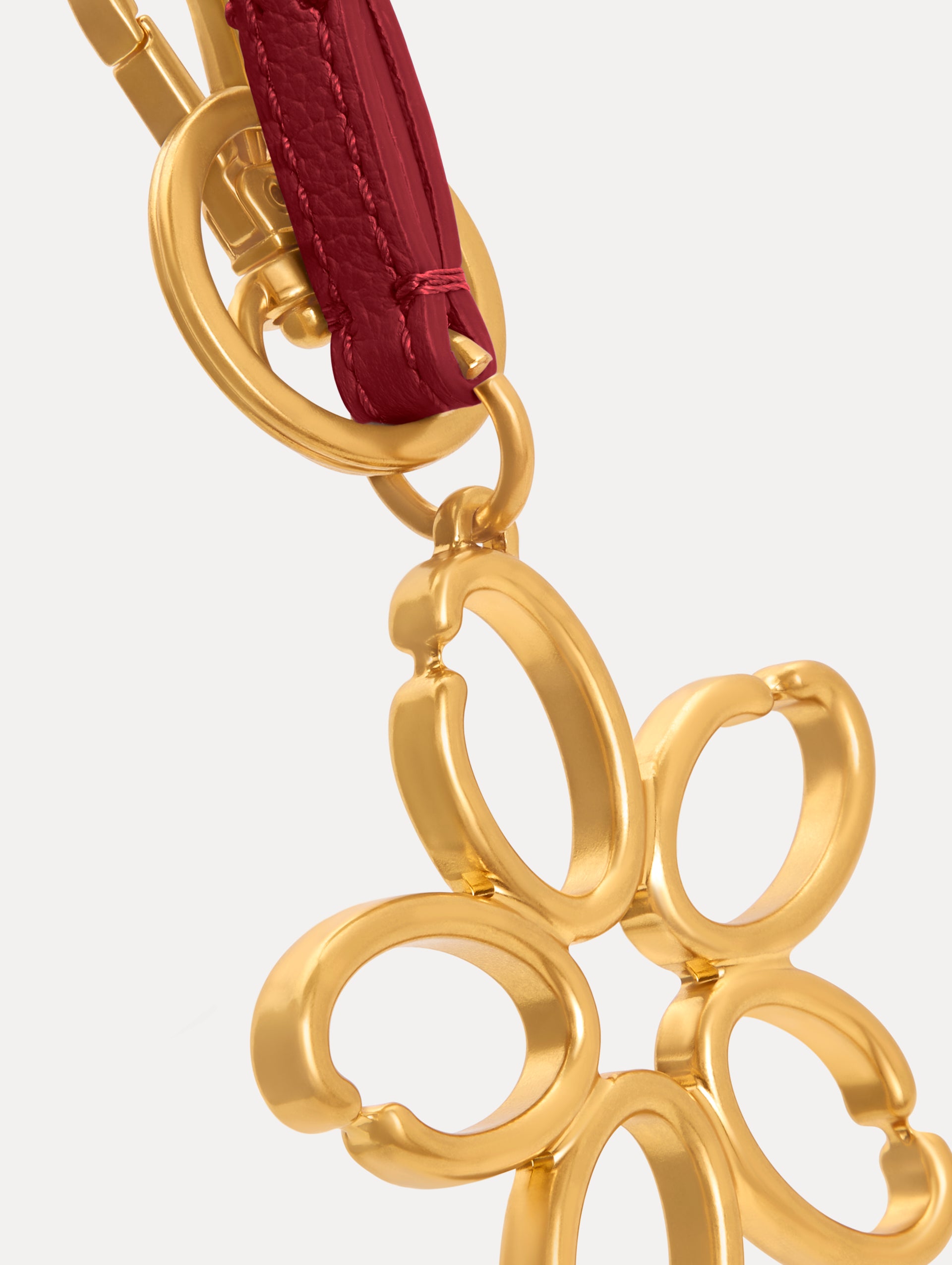 Gold O Flower Wristlet Key Chain with a five-petal open flower that hangs from a deep red leather loop strap, connected by a small gold ring and clasp. Zoom View. 