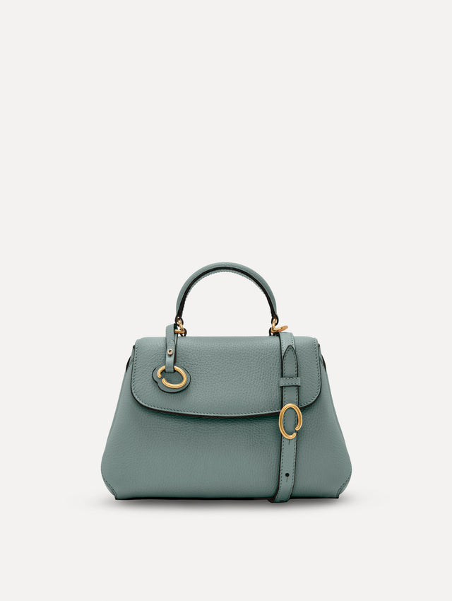 The Mini Poppy handbag in a Mint color with an Oscar O logo tag around the top handle, paired with a floral white dress. Front View.