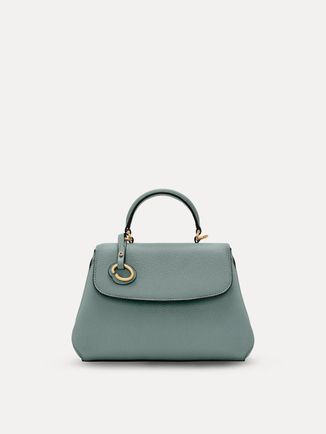 The Mini Poppy handbag in a Mint color with an Oscar O logo tag around the top handle, paired with a floral white dress. Front View.