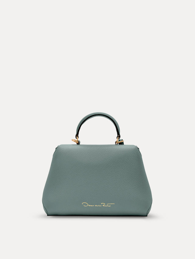 The Mini Poppy handbag in a Mint color with an Oscar O logo tag around the top handle, paired with a floral white dress. Back View.