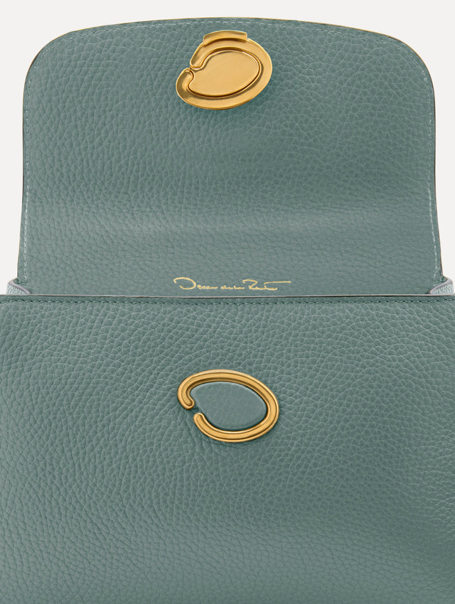 The Mini Poppy handbag in a Mint color with an Oscar O logo tag around the top handle, paired with a floral white dress. Zoom View.
