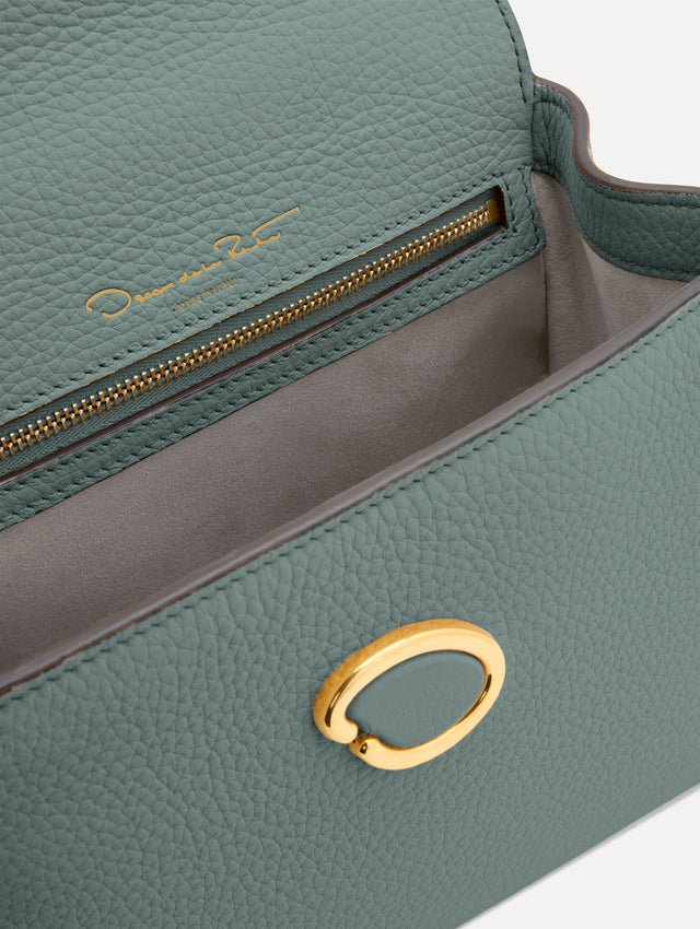 The Mini Poppy handbag in a Mint color with an Oscar O logo tag around the top handle, paired with a floral white dress. Zoom View.