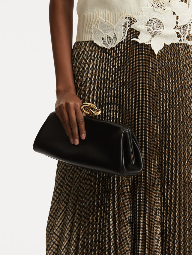 Model holding black clutch with gold 'O' emblem on the clasp. 