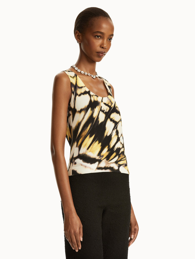 Model wearing Abstract butterfly print in yellow, black, and white tank, paired with black pants. Side view.