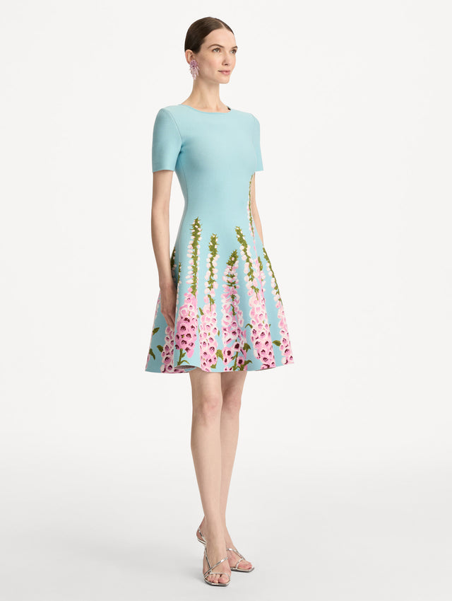 Blue Foxglove Jacquard Knit Dress with short sleeves, a fitted bodice, flared skirt, and pink foxglove floral embroidery cascading from the hem upward. Side View.