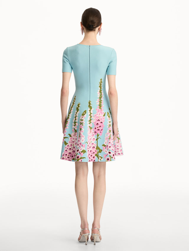Blue Foxglove Jacquard Knit Dress with short sleeves, a fitted bodice, flared skirt, and pink foxglove floral embroidery cascading from the hem upward. Back View.