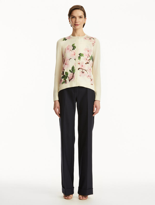 Model wearing white cardigan with pink cherry blossoms, paired with black pants. Front View