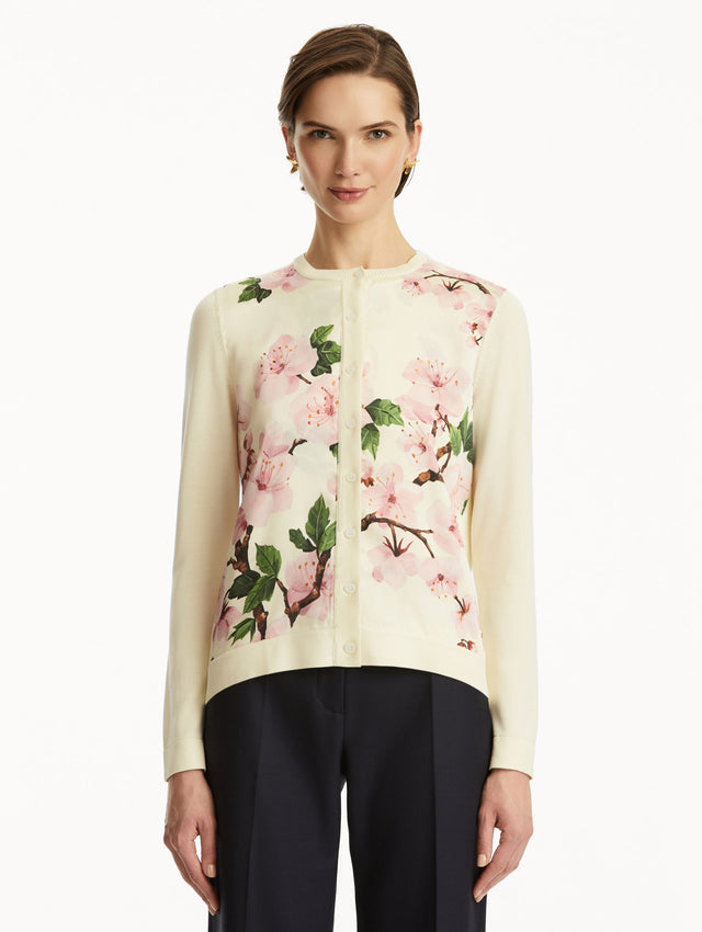 Model wearing white cardigan with pink cherry blossoms, paired with black pants. Front View