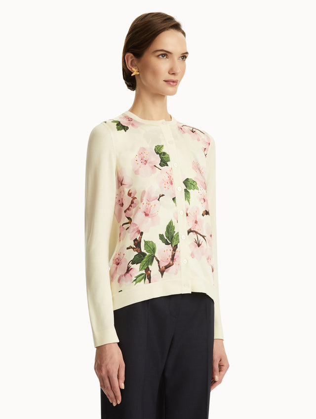 Model wearing white cardigan with pink cherry blossoms, paired with black pants. Side View