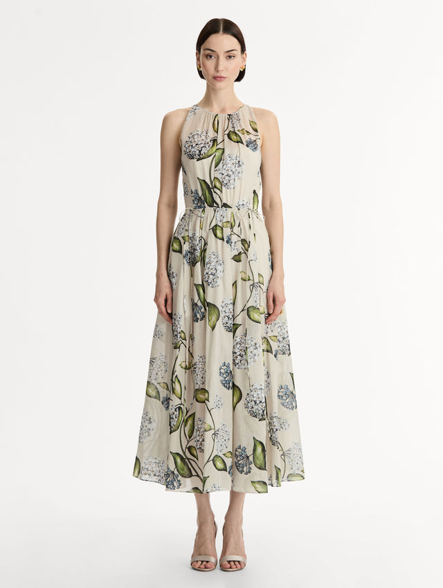 Halter neck, sleeveless, cotton poplin midi dress in off white. Pleated with blue flower print. Subtle bows at waist. Front View.