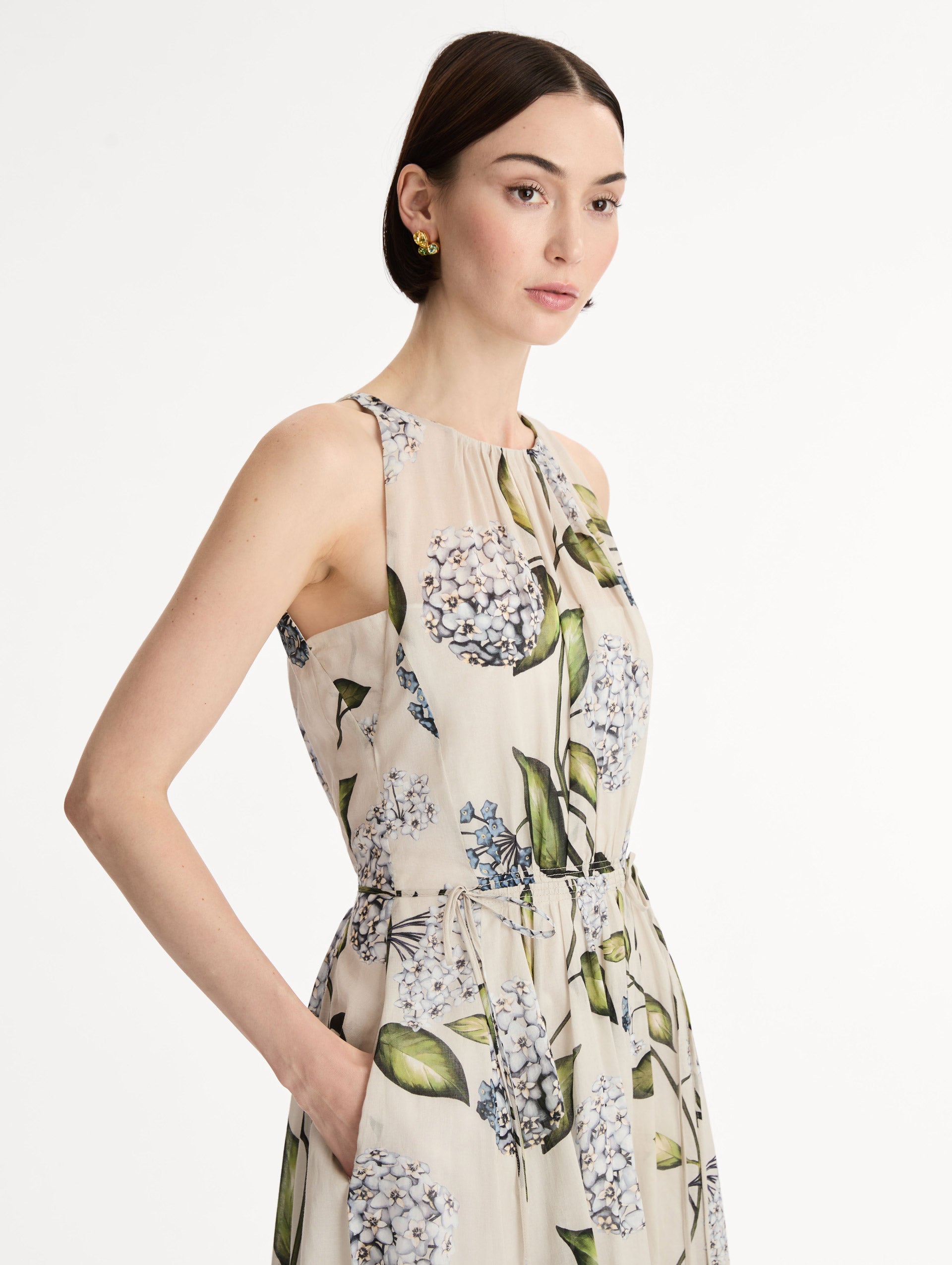 Halter neck, sleeveless, cotton poplin midi dress in off white. Pleated with blue flower print. Subtle bows at waist. Side View.
