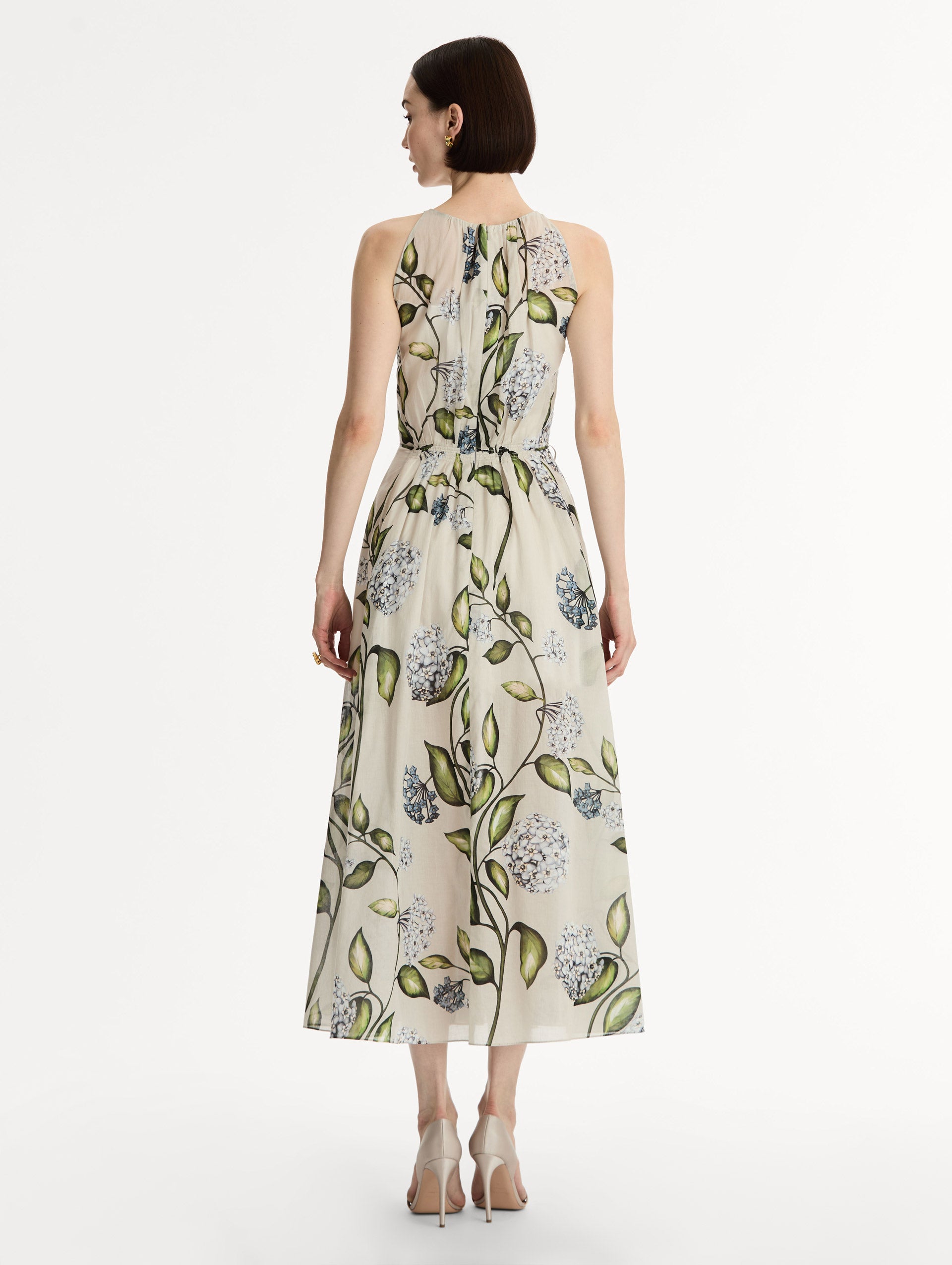 Halter neck, sleeveless, cotton poplin midi dress in off white. Pleated with blue flower print. Subtle bows at waist. Back View.