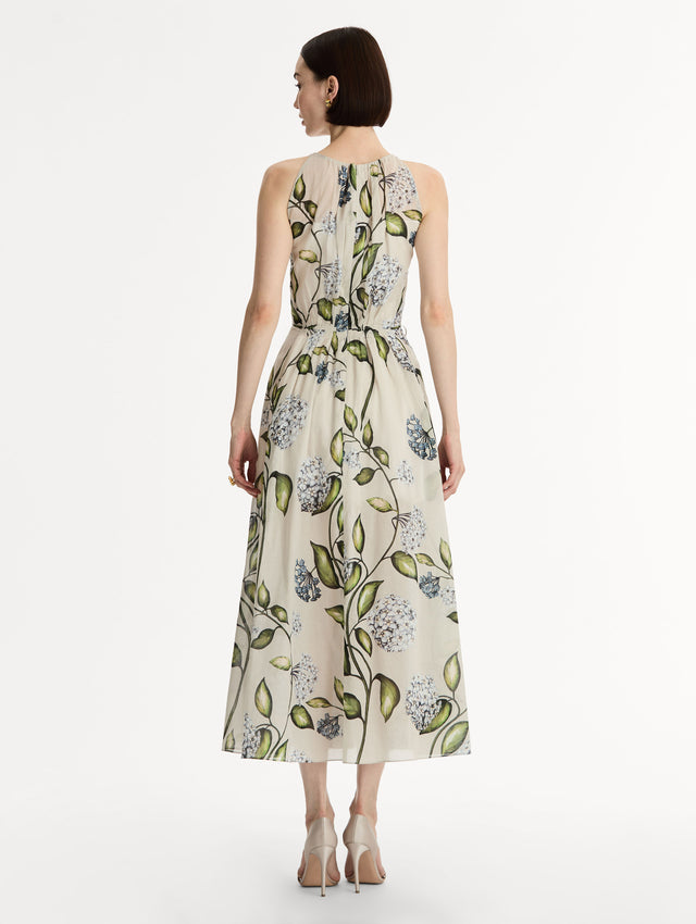 Halter neck, sleeveless, cotton poplin midi dress in off white. Pleated with blue flower print. Subtle bows at waist. Back View.