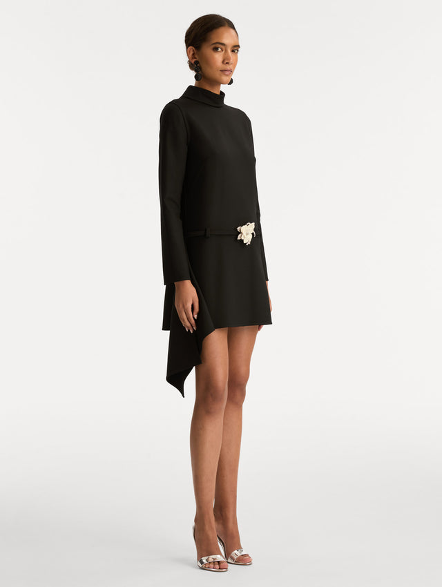 Black Floral Belt Mock-Neck Dress featuring a belt with a white flower and a black drape detail. Side View.