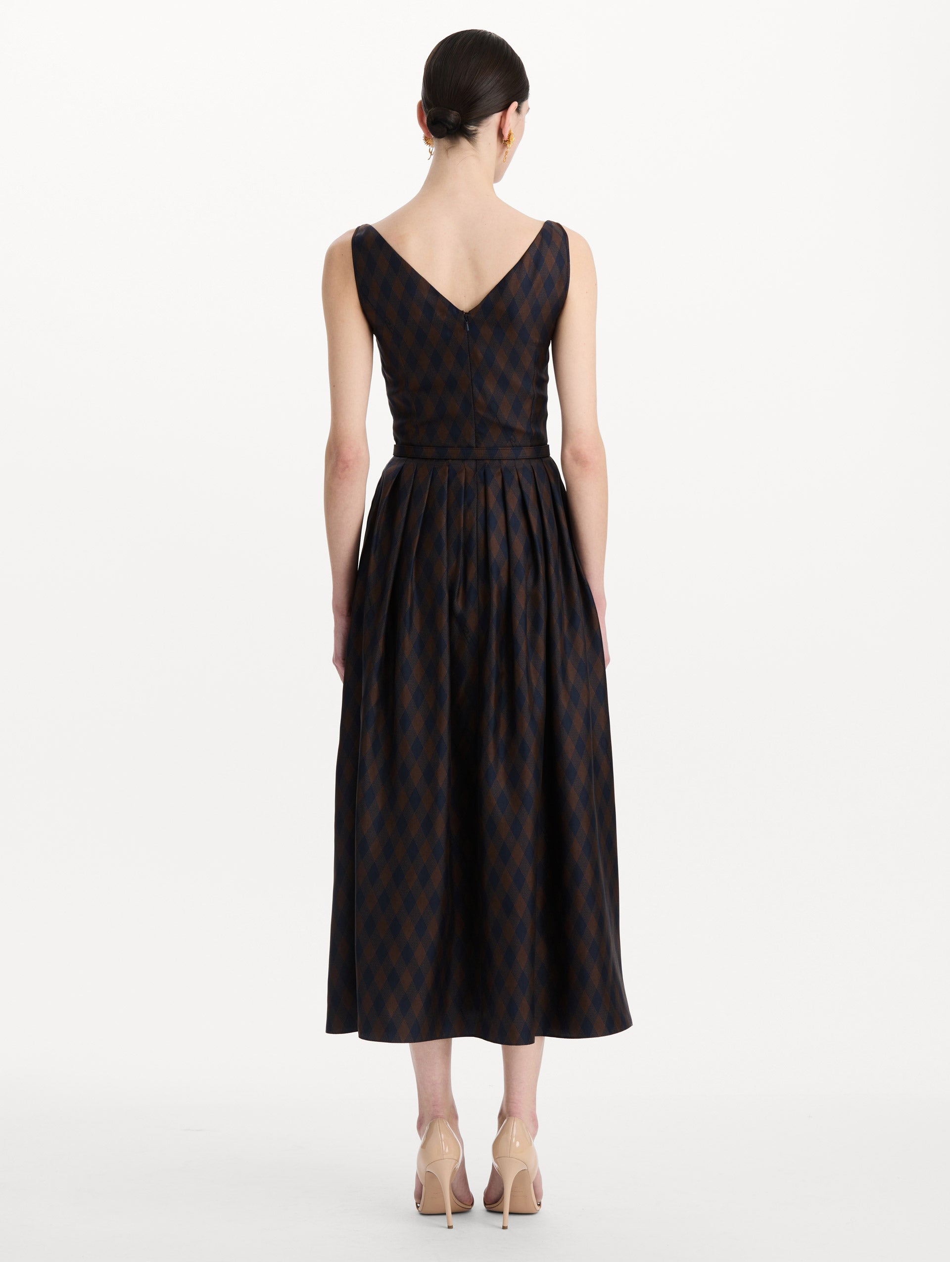 The model is wearing the argyle silk twill dress with a sleeveless silhouette, a V-neckline, and an argyle print in navy and brown. Back view. 