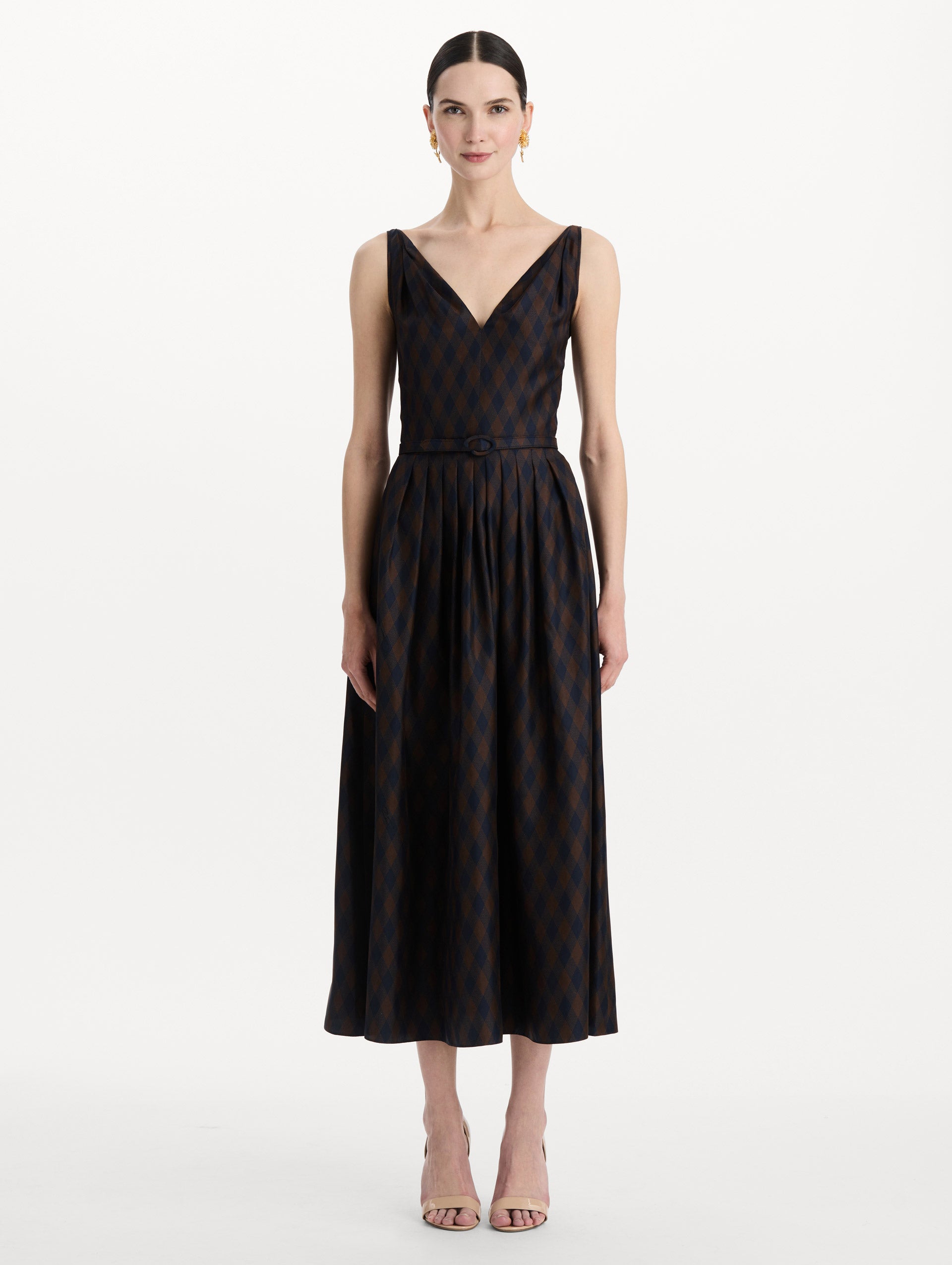 The model is wearing the argyle silk twill dress with a sleeveless silhouette, a V-neckline, and an argyle print in navy and brown. Front view. 