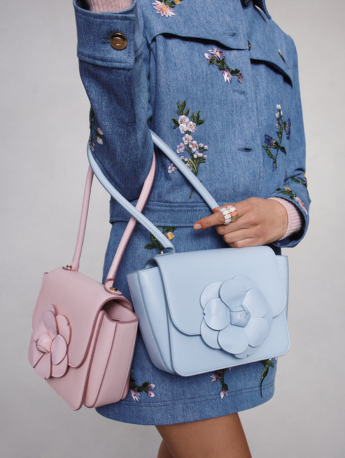 The model is wearing a denim jacket and skirt paired with two Top Handle TRO Bags in blush and sky blue. 

