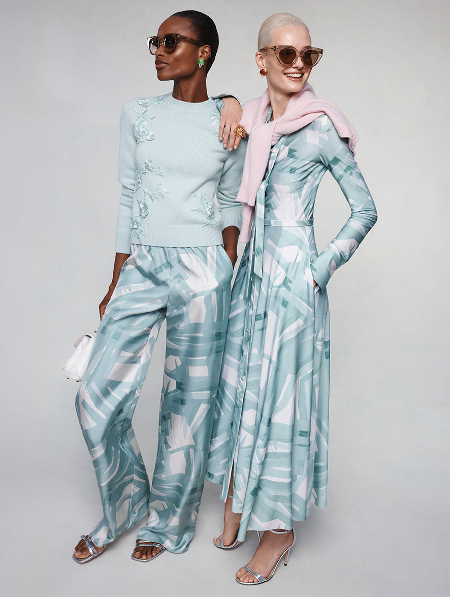 Two models pose in Pre-Spring 2027 outfits that feature the Stripey Plaid family. The model to the left is wearing a turquoise pullover knit paired with patterned pants. The model the right is wearing a patterned long sleeve day dress with a blush sweater at shoulders. 
