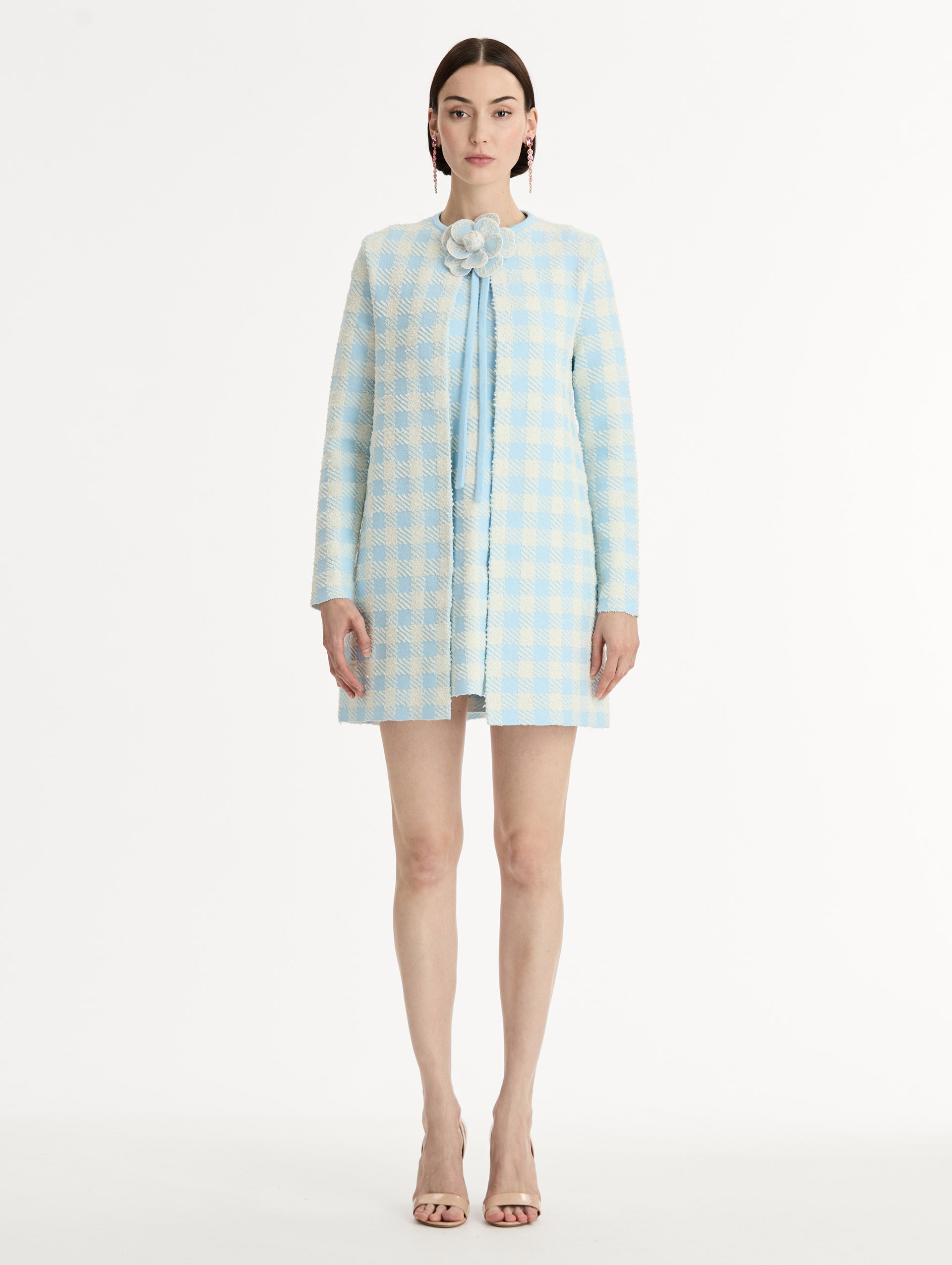 Textured jacquard, long sleeve coat in pale blue and ivory gingham pattern. Streamlined silhouette with a floral appliqué at the neckline. Front View. 