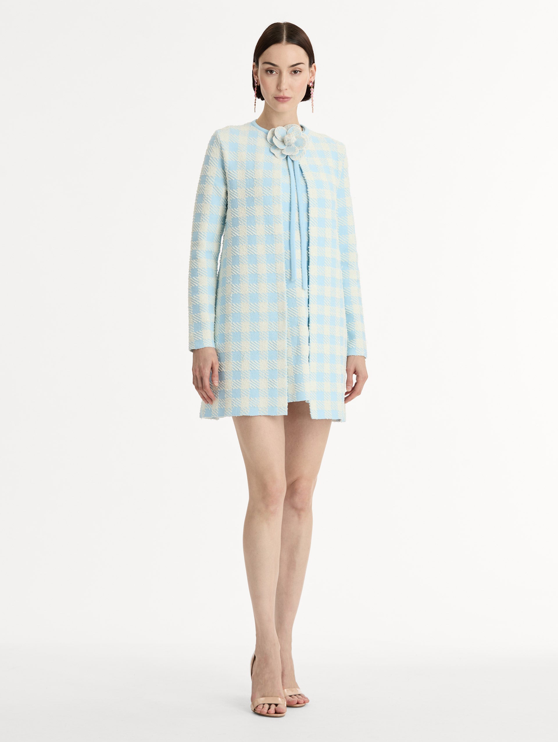 Textured jacquard, long sleeve coat in pale blue and ivory gingham pattern. Streamlined silhouette with a floral appliqué at the neckline. Side View. 