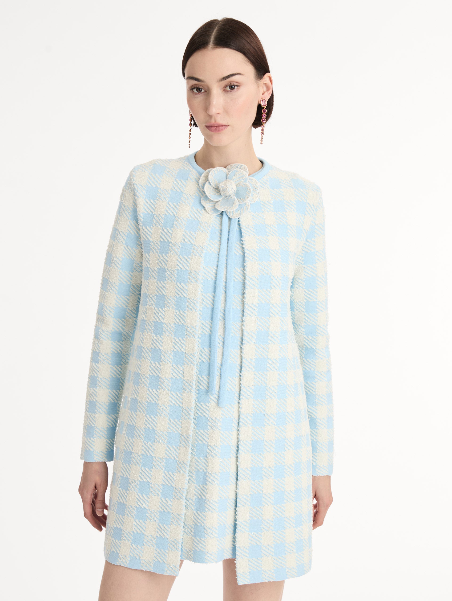 Textured jacquard, long sleeve coat in pale blue and ivory gingham pattern. Streamlined silhouette with a floral appliqué at the neckline. Front View, Close Up. 