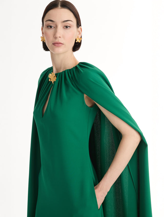 Emerald georgette caftan with fluid silhouette. Singular gilded cyclamen detail offers a sculptural focal point. Sweeping cape-like shape. Front View, Close up.