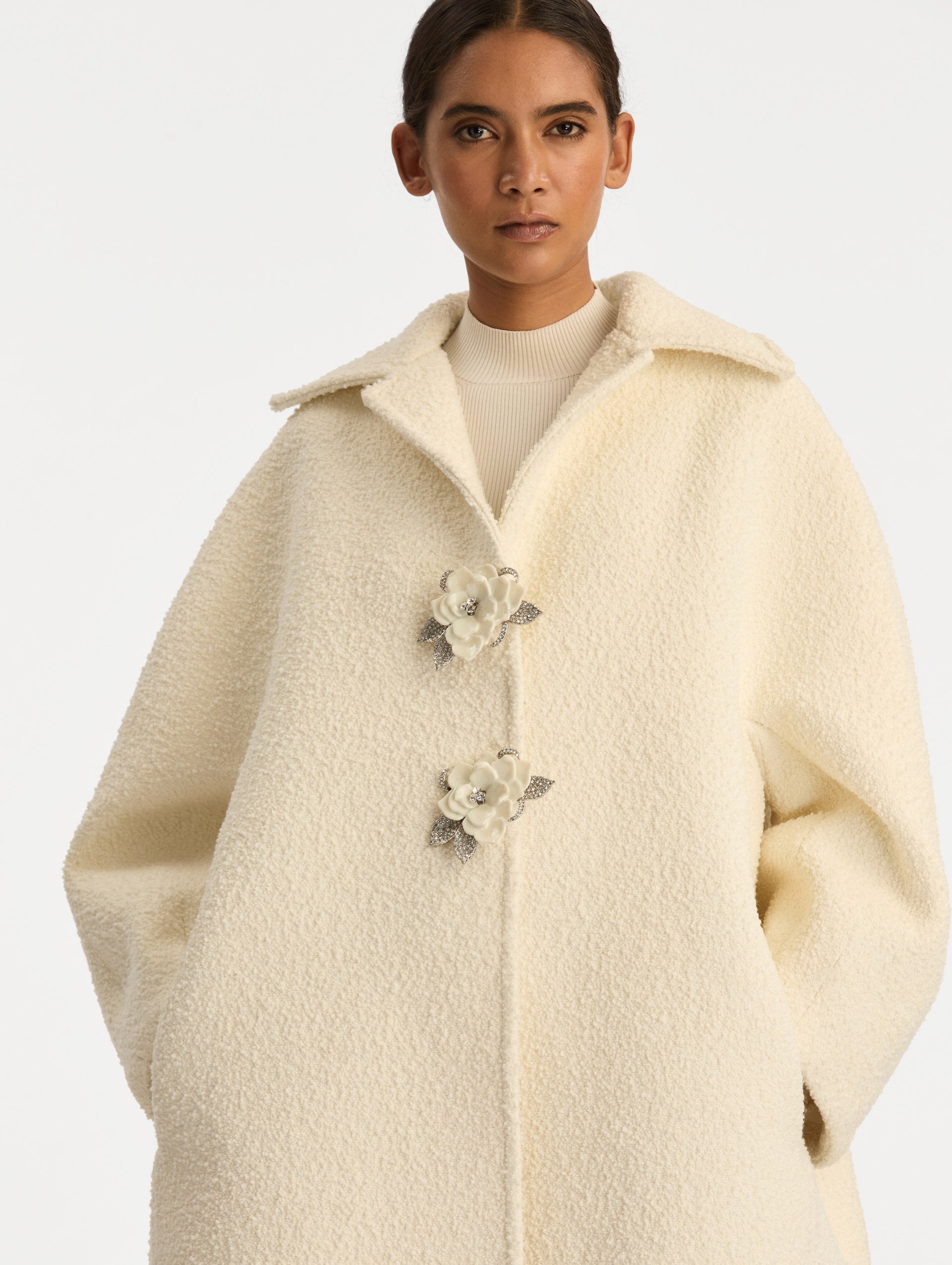 Ivory Floral Button Bouclé Tweed Coat with notched lapels, featuring two floral crystal-embellished clasps at the front. Zoom View.
