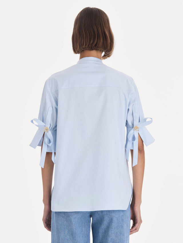 The model is wearing a short sleeve cotton poplin sateen blouse. Back view.