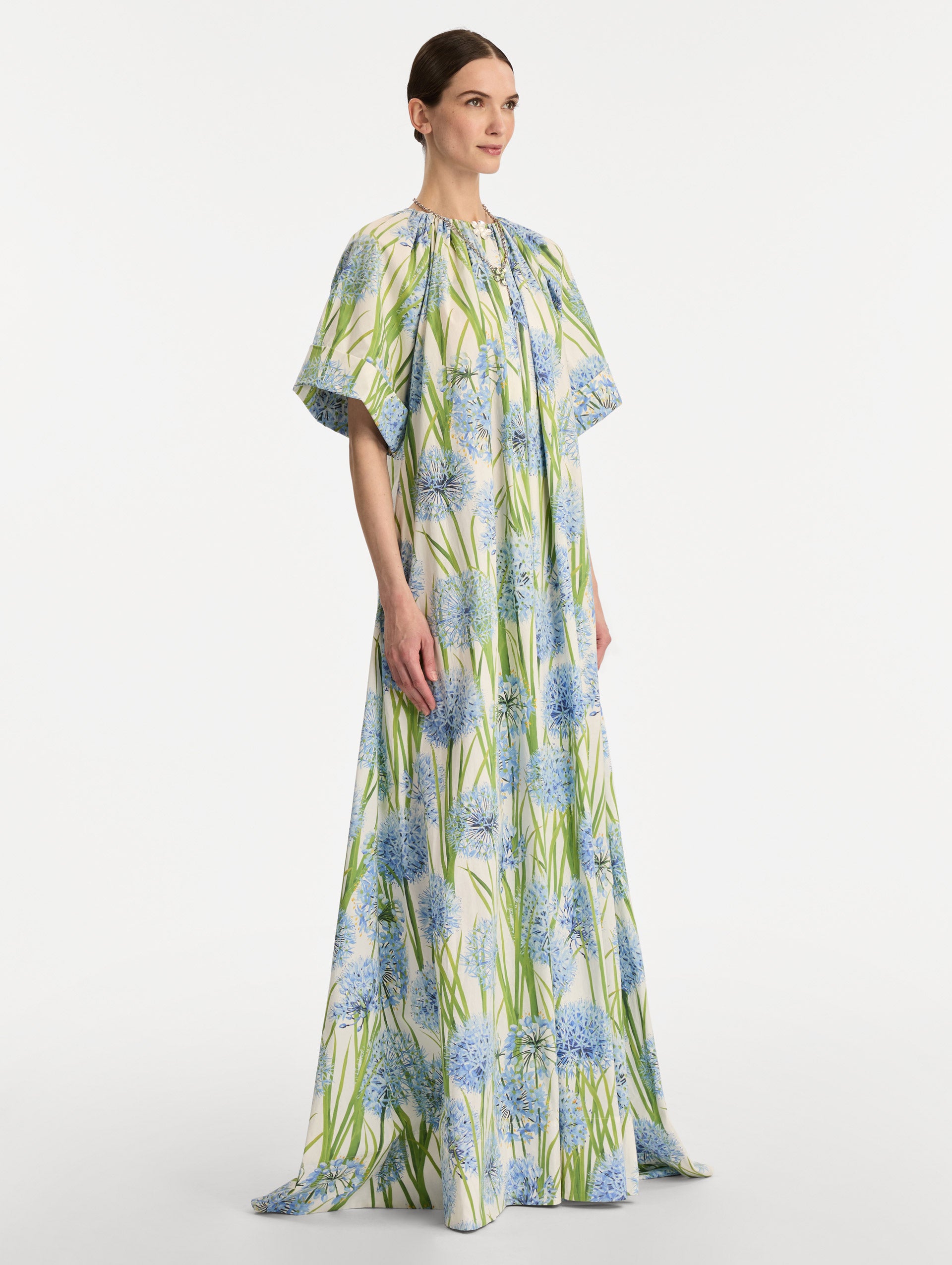 Ivory Allium Cotton Poplin Caftan with short sleeves and gathered neckline, featuring an allover blue floral print with green stems. Side View.
