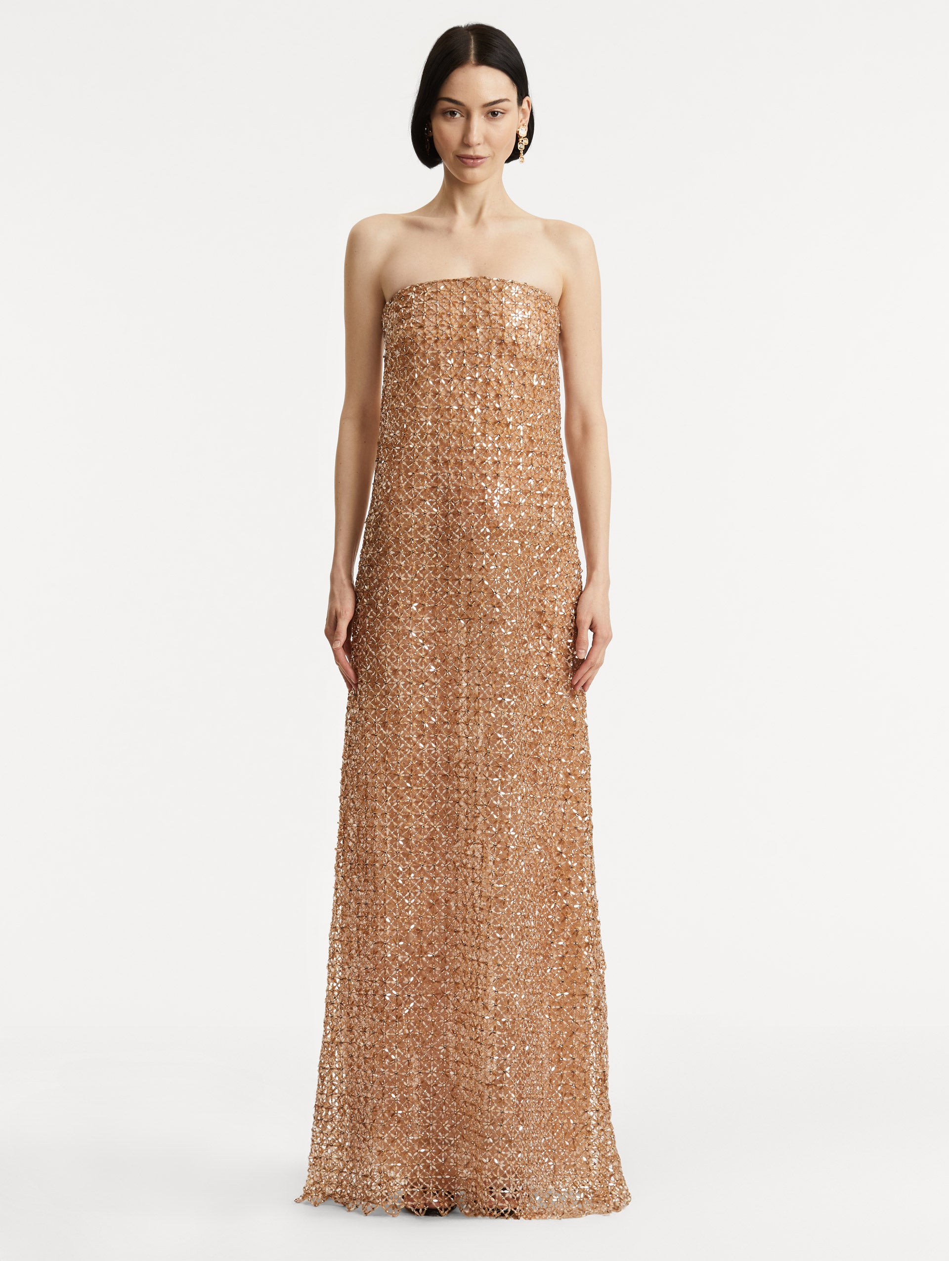 Full body front view of model wearing amber-hued strapless gown with a column silhouette glass floral embroidery in a grid pattern. 