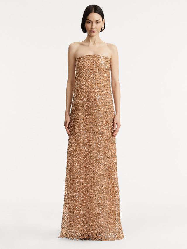 Full body front view of model wearing amber-hued strapless gown with a column silhouette glass floral embroidery in a grid pattern. 