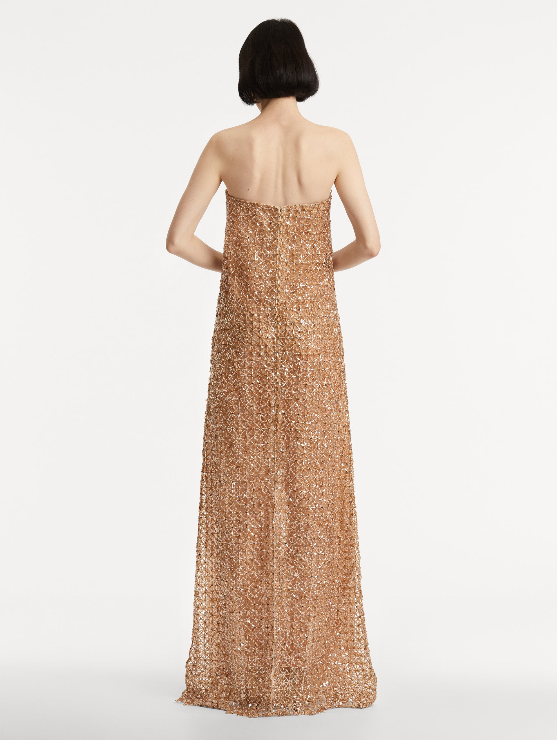 Full body back view of model wearing amber-hued strapless gown with a column silhouette glass floral embroidery in a grid pattern. 