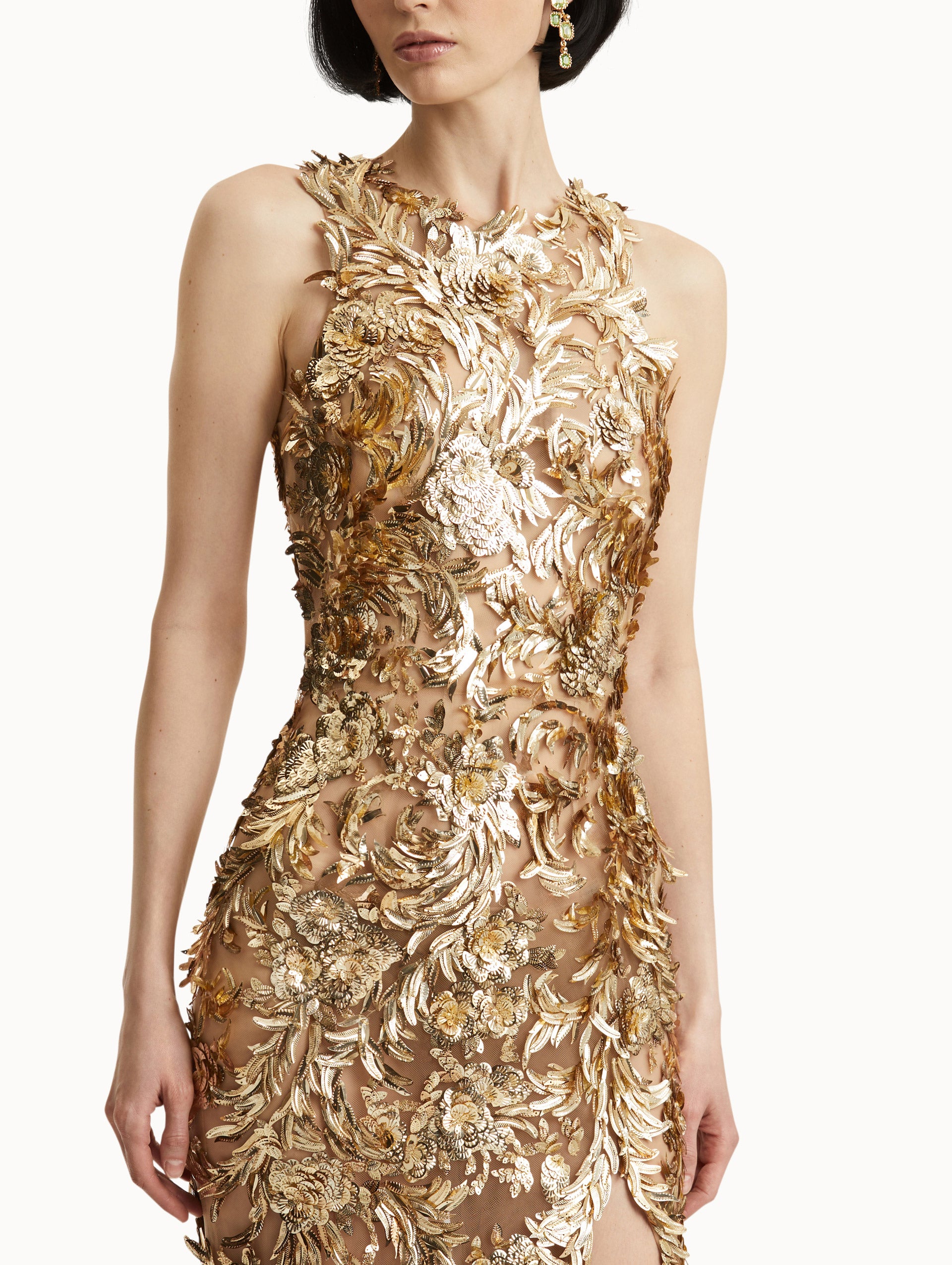 Zoomed in image of model wearing sleeveless gold-embroidered gown with feathers unfurling across a tulle base. 