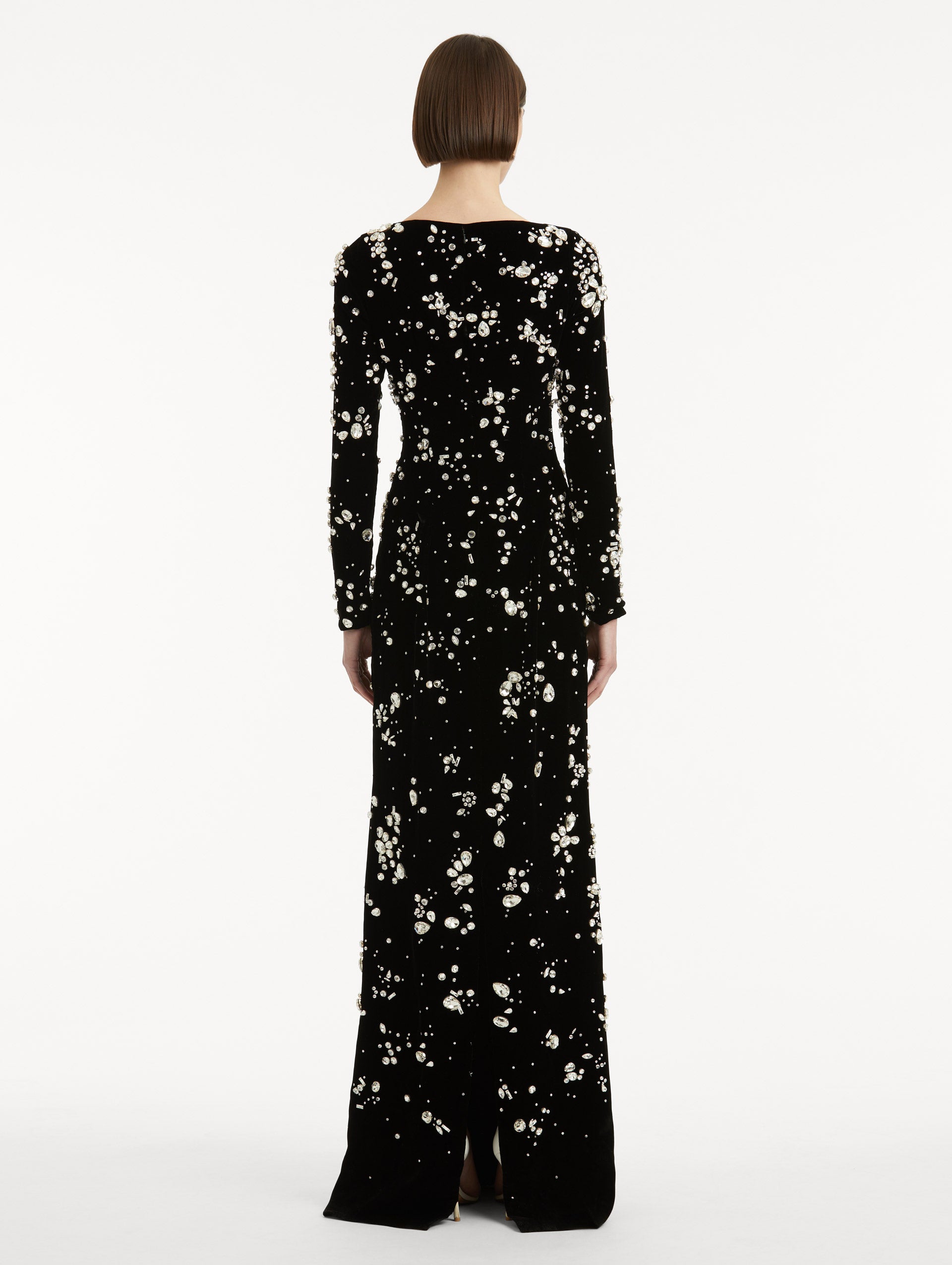Full body back view of model wearing a long sleeve black gown with multi-dimensional stones scattered across the dress, features column silhouette.