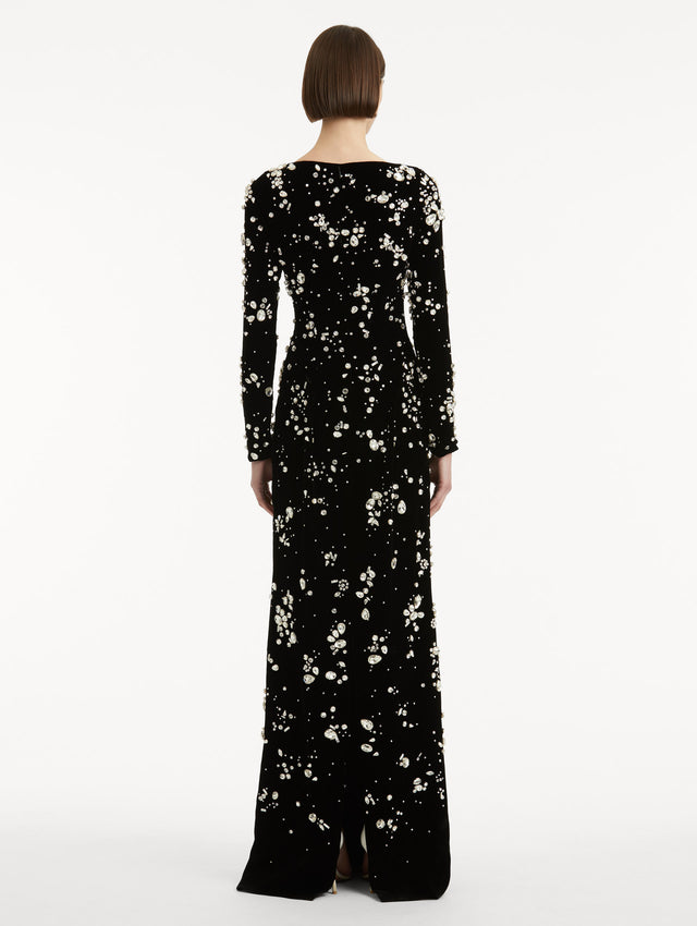 Full body back view of model wearing a long sleeve black gown with multi-dimensional stones scattered across the dress, features column silhouette.
