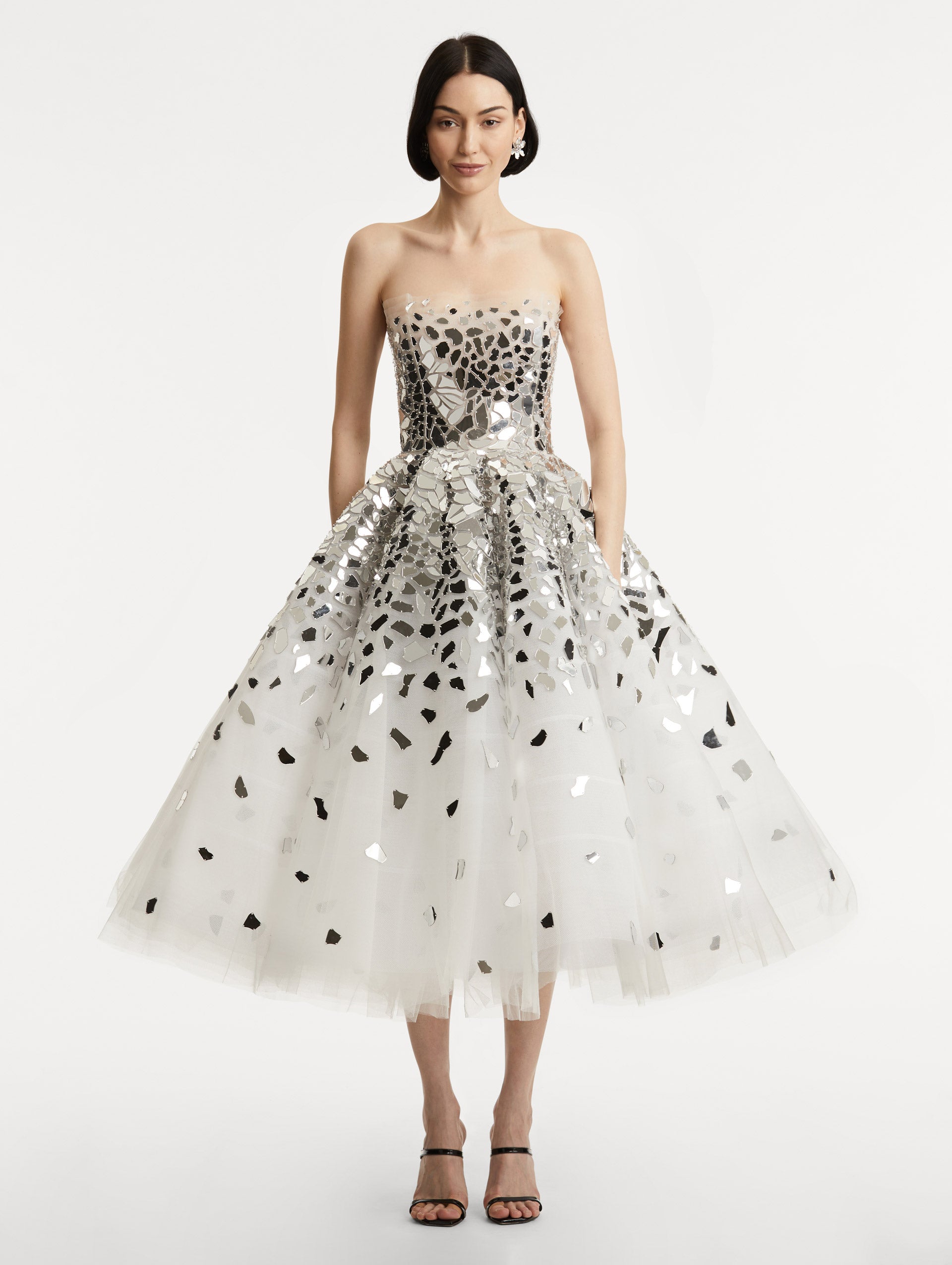 Full body front view of model wearing strapless dress with a white tulle base, mirrored mosaic pieces concentrated on bodice and fade down the skirt