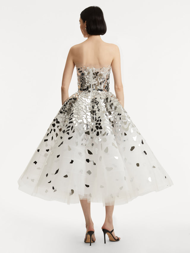 Full body back view of model wearing strapless dress with a white tulle base, mirrored mosaic pieces concentrated on bodice and fade down the skirt
