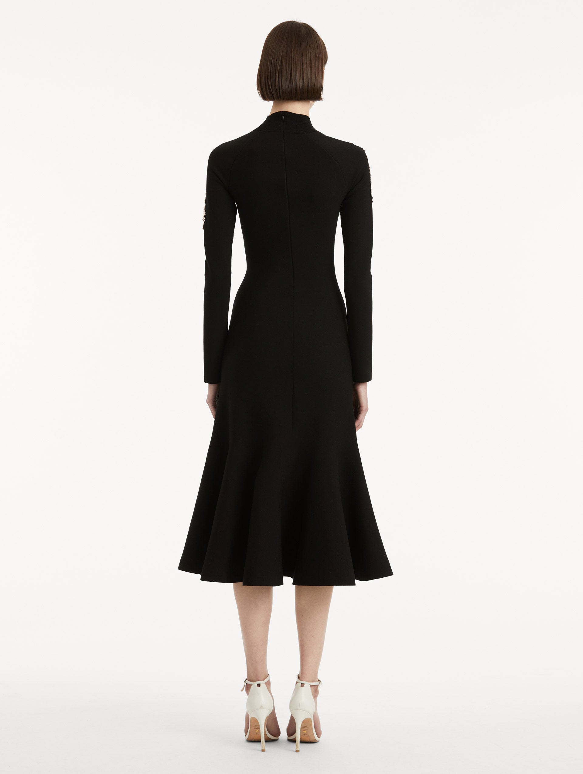 Full body back view image of model wearing a black long sleeve dress with a mock neckline and flared skirt. 