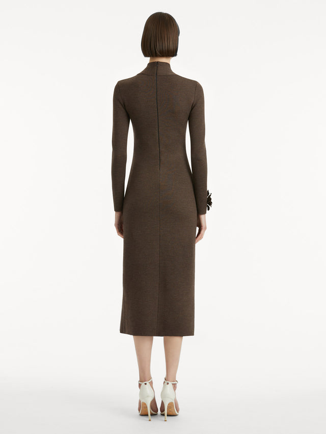Full body back view of model wearing a long sleeve dark brown dress with a pencil silhouette and mock neckline. Tonal peony appliqués, with beaded detailing, frame the and sleeves and features a black zipper.