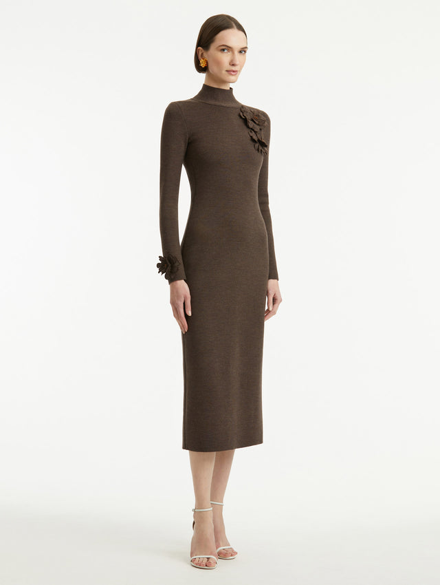Full body side view of model wearing a long sleeve dark brown dress with a pencil silhouette and mock neckline. Tonal peony appliqués, with beaded detailing, frame the neckline and sleeves.