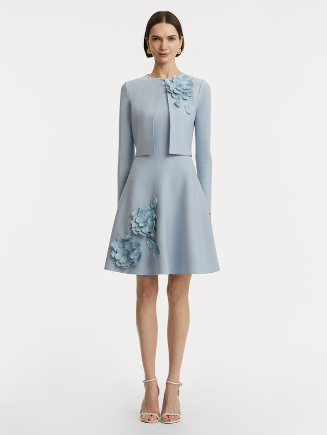 Full body front view of model wearing a cropped overlayer in light blue with sequin peony appliqués at the neckline. 