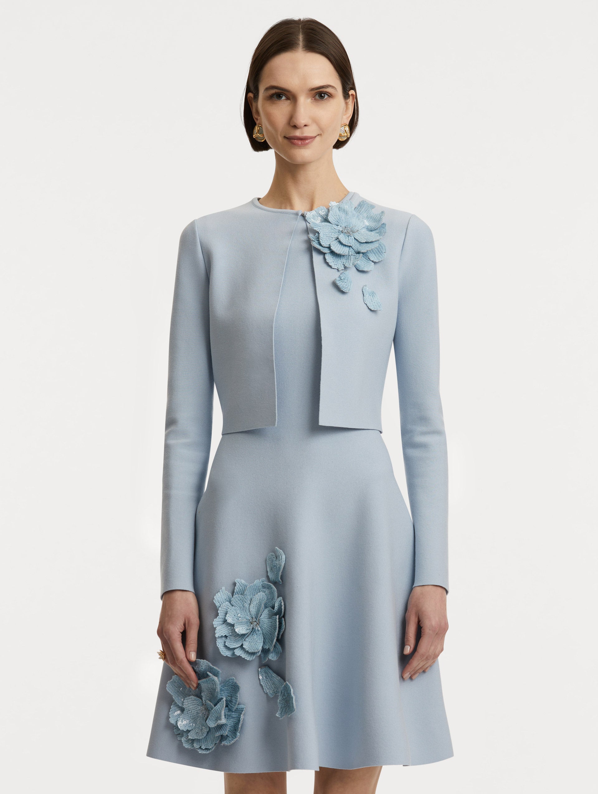 Front view of model wearing a cropped overlayer in light blue with sequin peony appliqués at the neckline. 